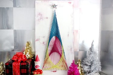 A blue, pink, and yellow string art tree on a white background