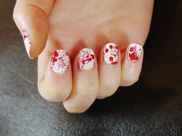 Red blood splatter polish on white nails.