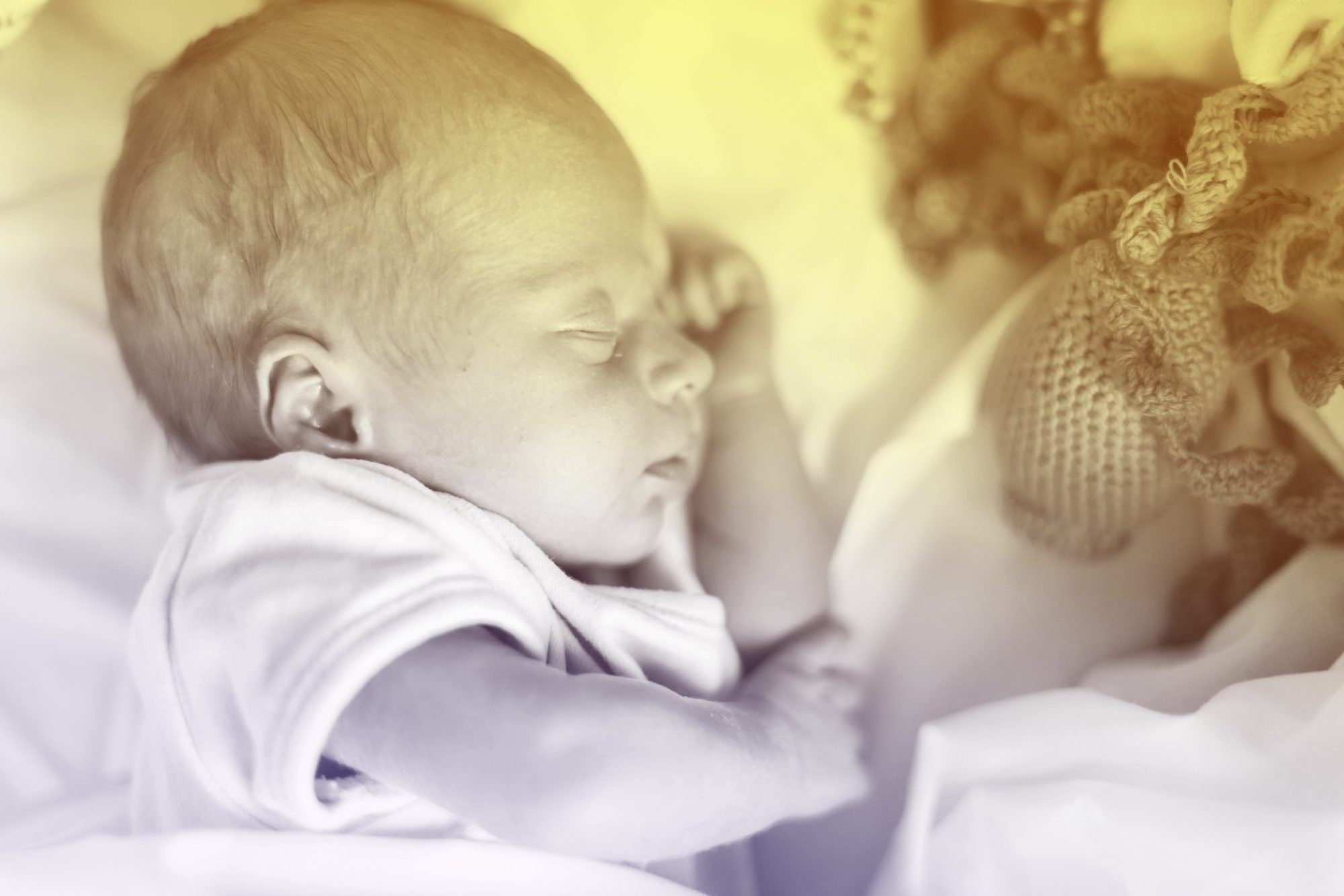 Close-up photograph of a newborn sleeping in his crib with his toys